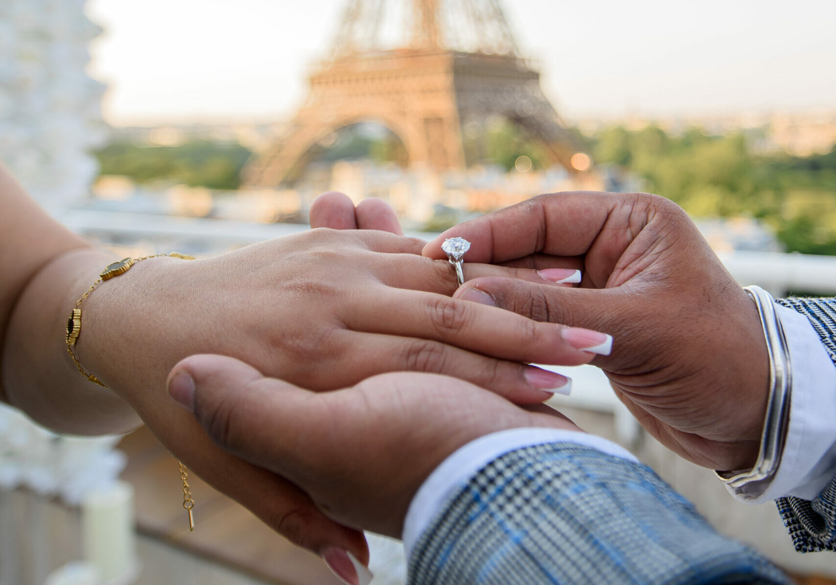 man sliding a diamond solitaire engagement ring onto a woman's finger with the Eiffel Tower in the background, captured during a romantic marriage proposal in Paris