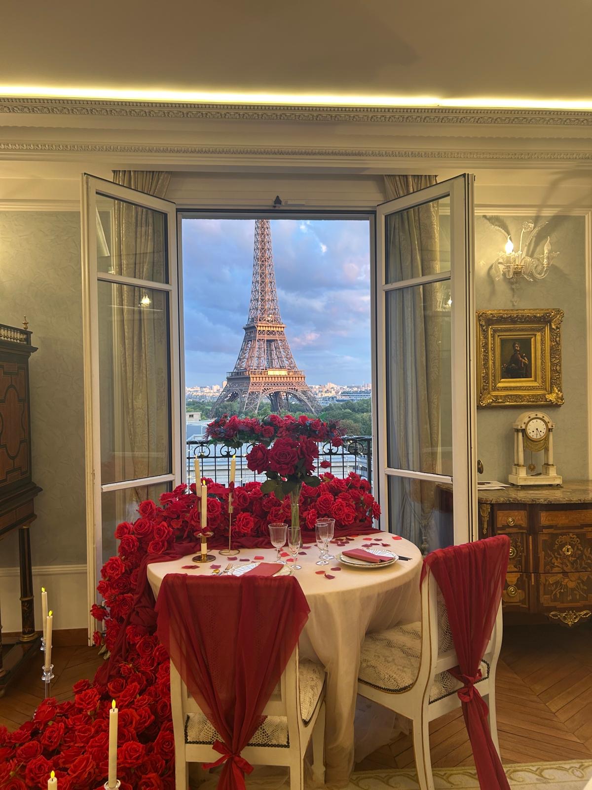 Private dinner table decorated with red roses and candles in a Haussmann apartment on Avenue du Président Wilson, with a full view of the Eiffel Tower through open French windows