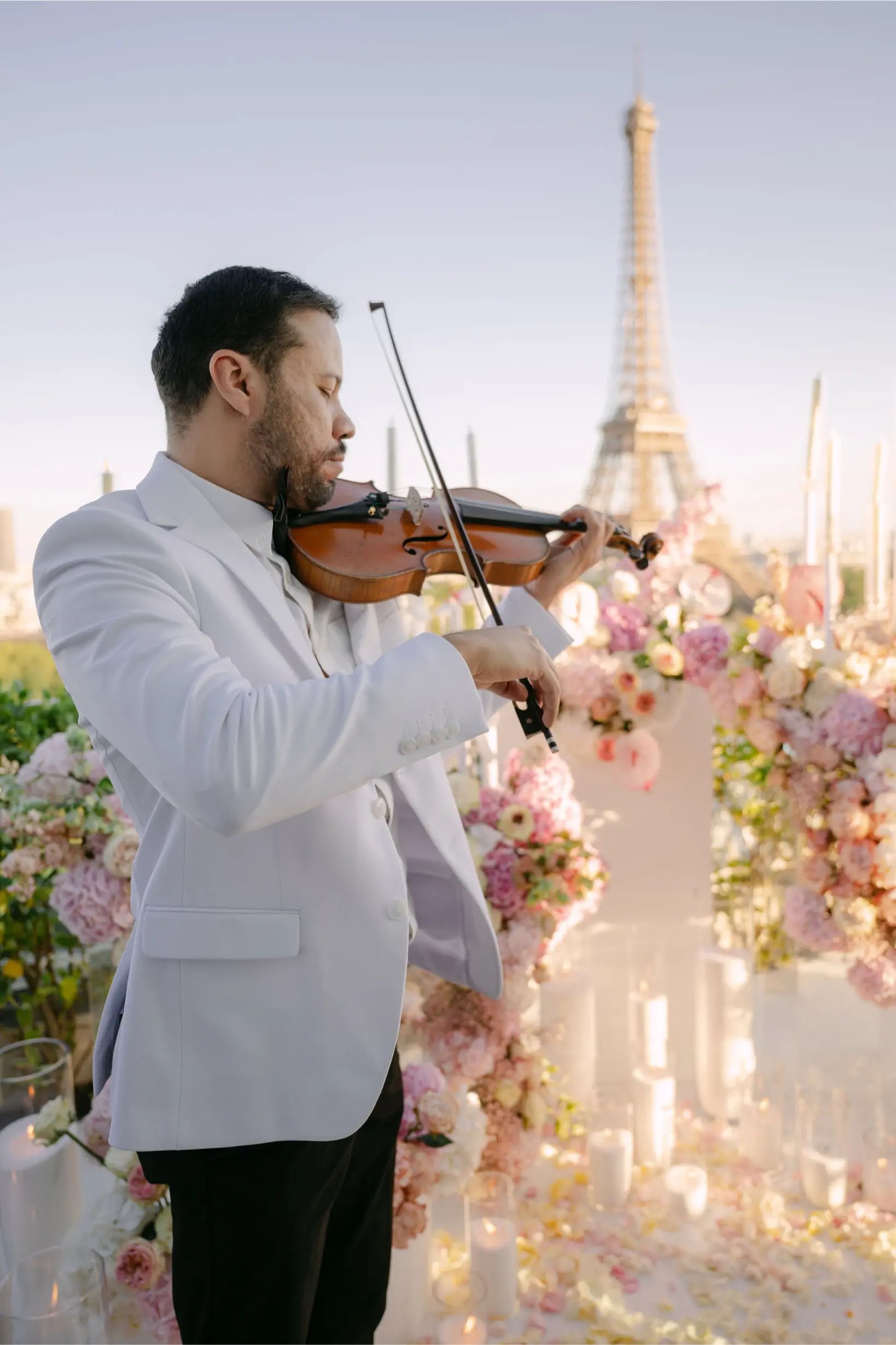 Violoniste en costume blanc jouant lors d'une demande en mariage sur rooftop privatisé à Paris, décoration florale rose et Tour Eiffel en arrière-plan