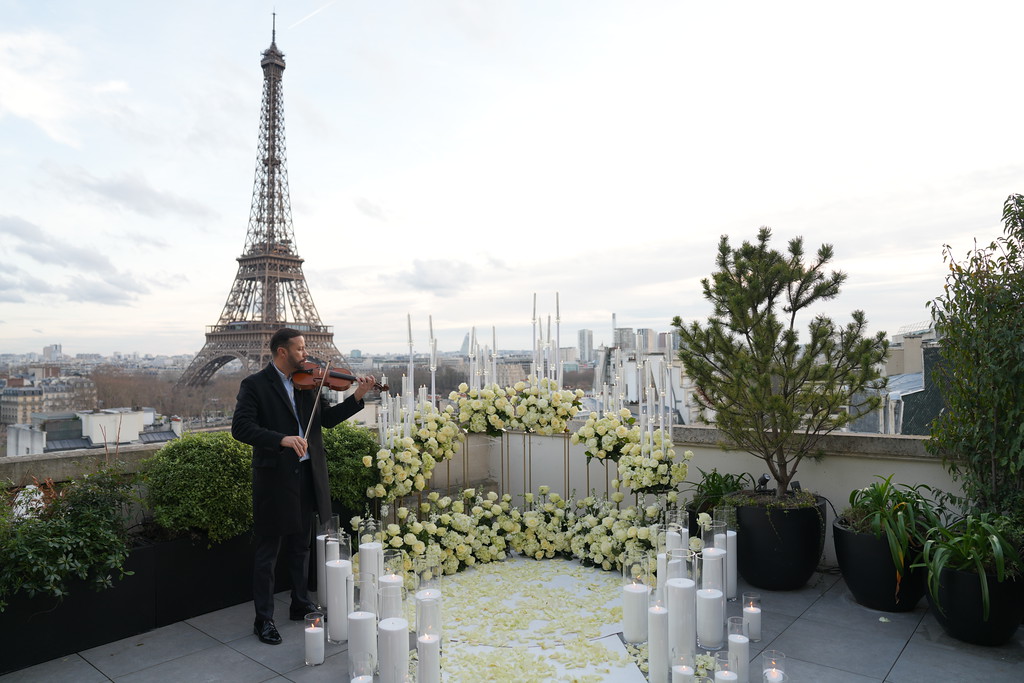 Décoration florale blanche et bougies sur un rooftop privatisé à Paris avec vue sur la Tour Eiffel, violoniste en live pour une demande en mariage
