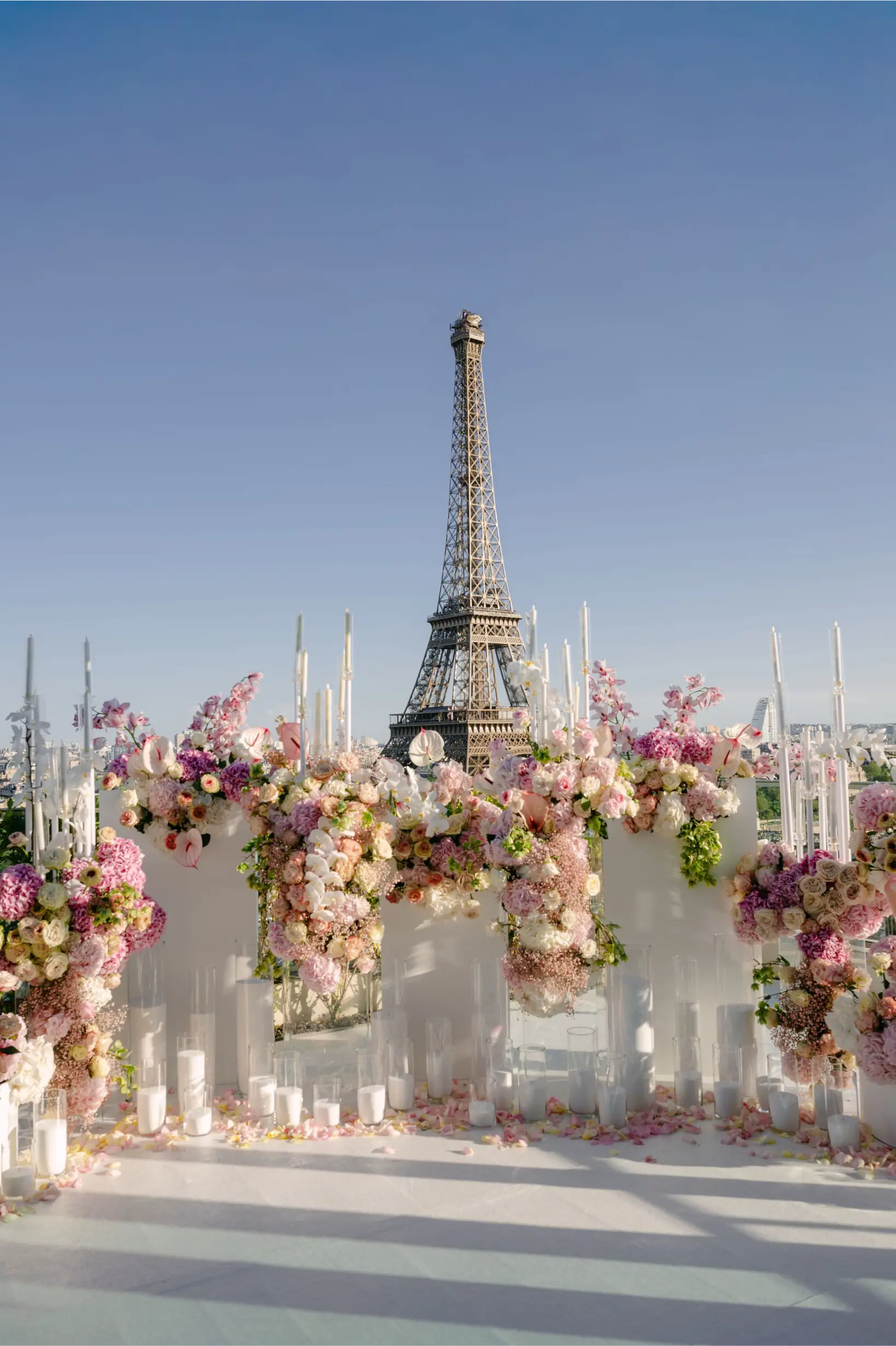 Décoration florale luxueuse rose et blanche avec arche fleurie, bougies et pétales sur un rooftop face à la Tour Eiffel pour une demande en mariage à Paris