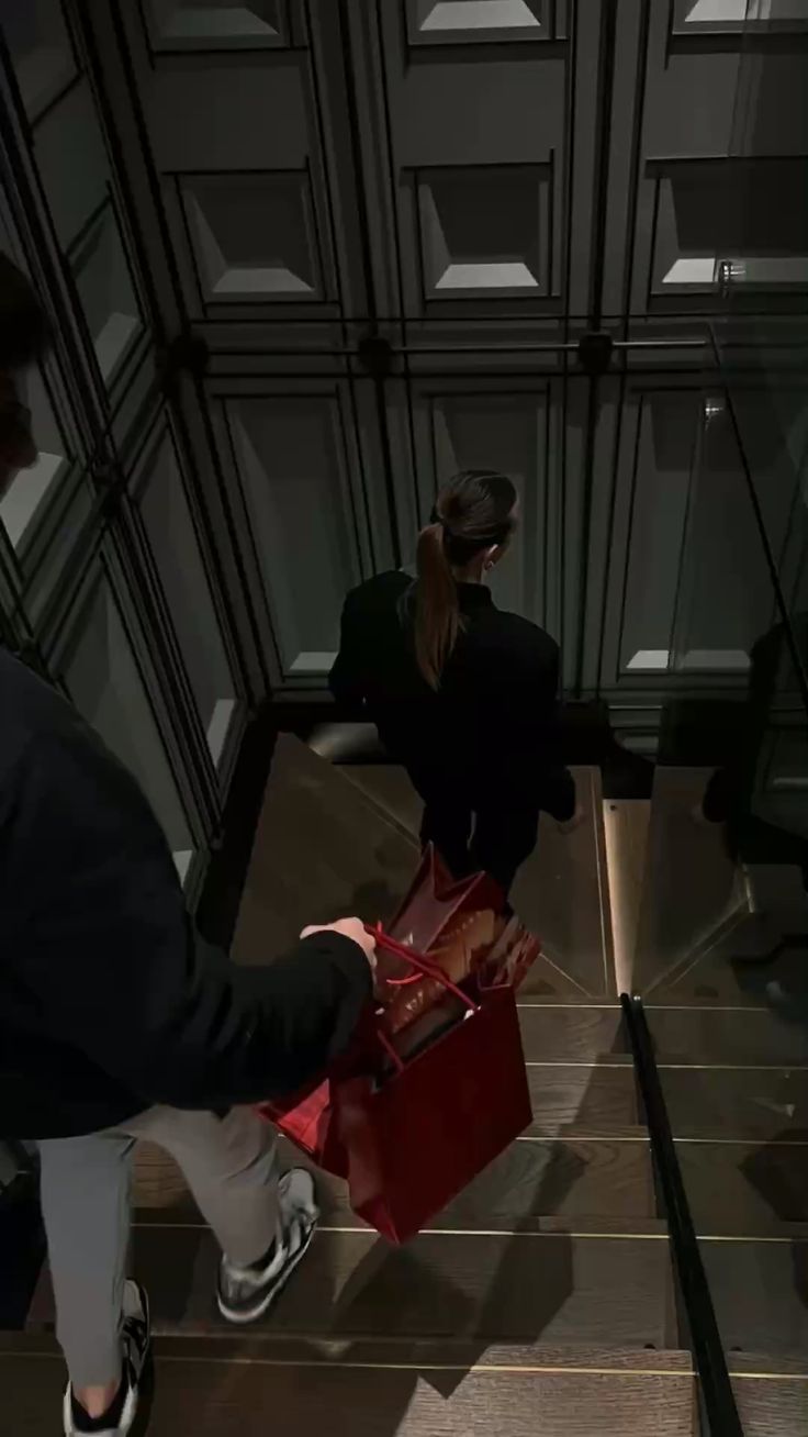 A man carrying red shopping bags while following a woman up the stairs of a luxury hotel or boutique