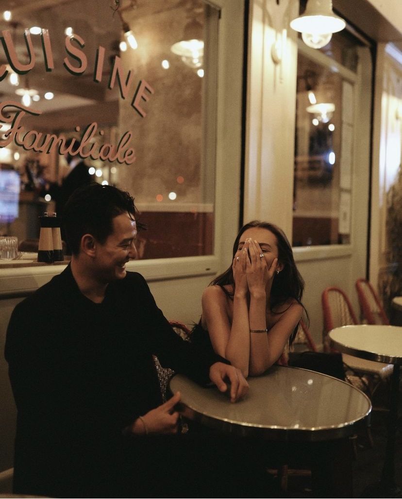 A couple laughing together at a Parisian café terrace in the evening.