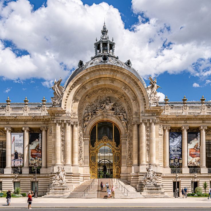Frontal view of the Petit Palais in Paris on a sunny day, showcasing its ornate Beaux-Arts facade with a grand arched entrance, gilded iron gates, intricate stone sculptures, decorative columns, and a sculpted dome against a blue sky with white clouds