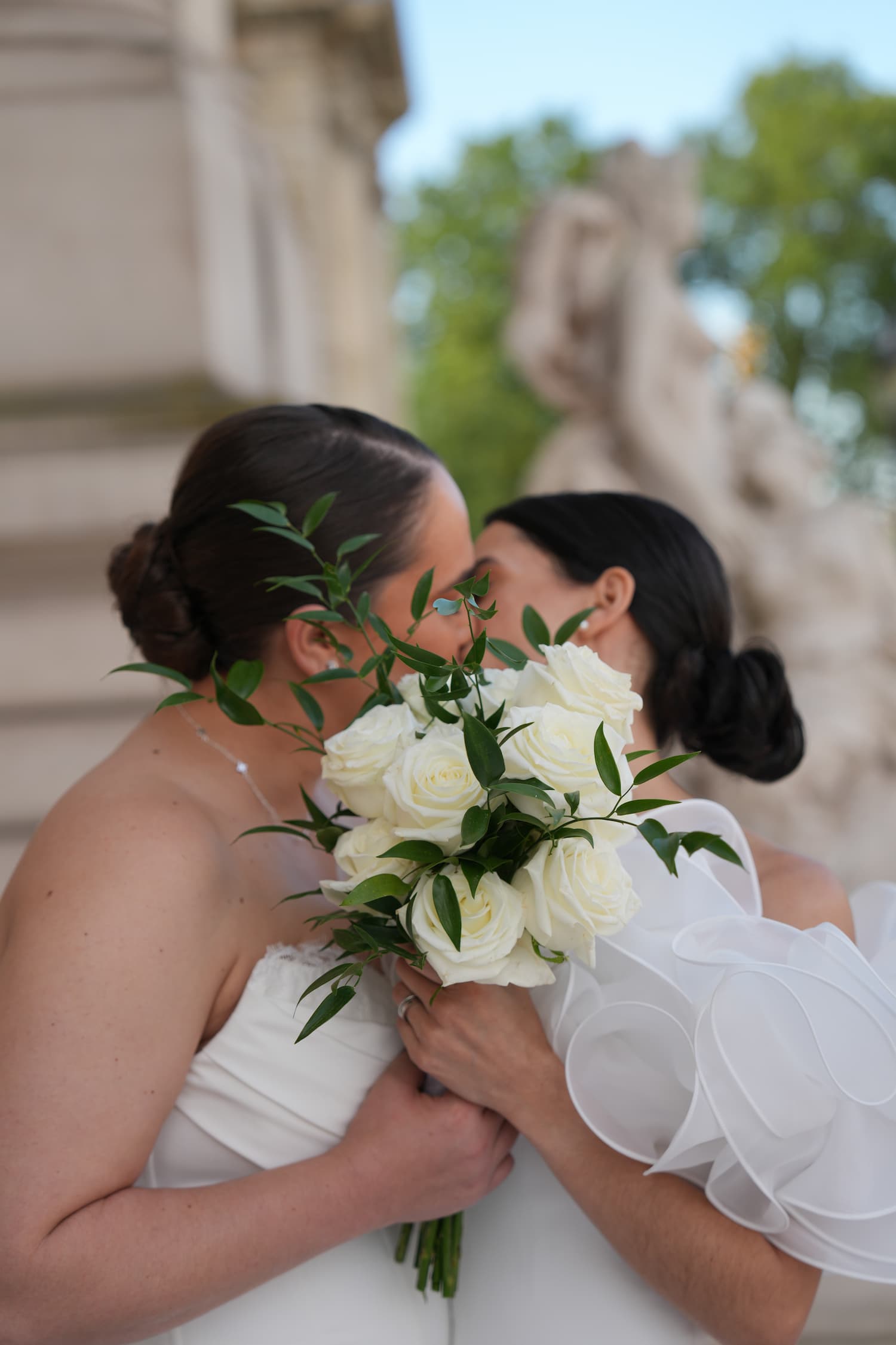Two brides sharing an intimate close moment behind a white rose bouquet at their Paris elopement
