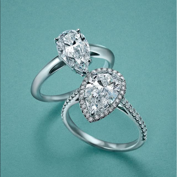 Two Tiffany & Co. platinum engagement rings with pear-cut diamonds side by side — one solitaire and one with a diamond halo and pavé band — elegant choices for a Paris engagement
