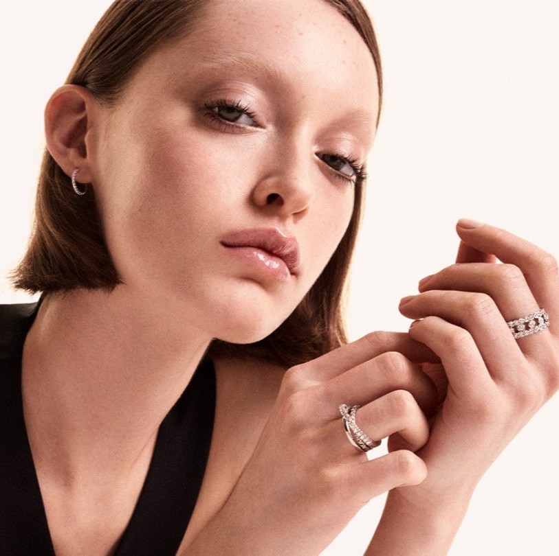 A woman wearing multiple diamond rings stacked on her fingers alongside delicate diamond hoop earrings, showcasing elegant jewellery options for an engagement ring in Paris.