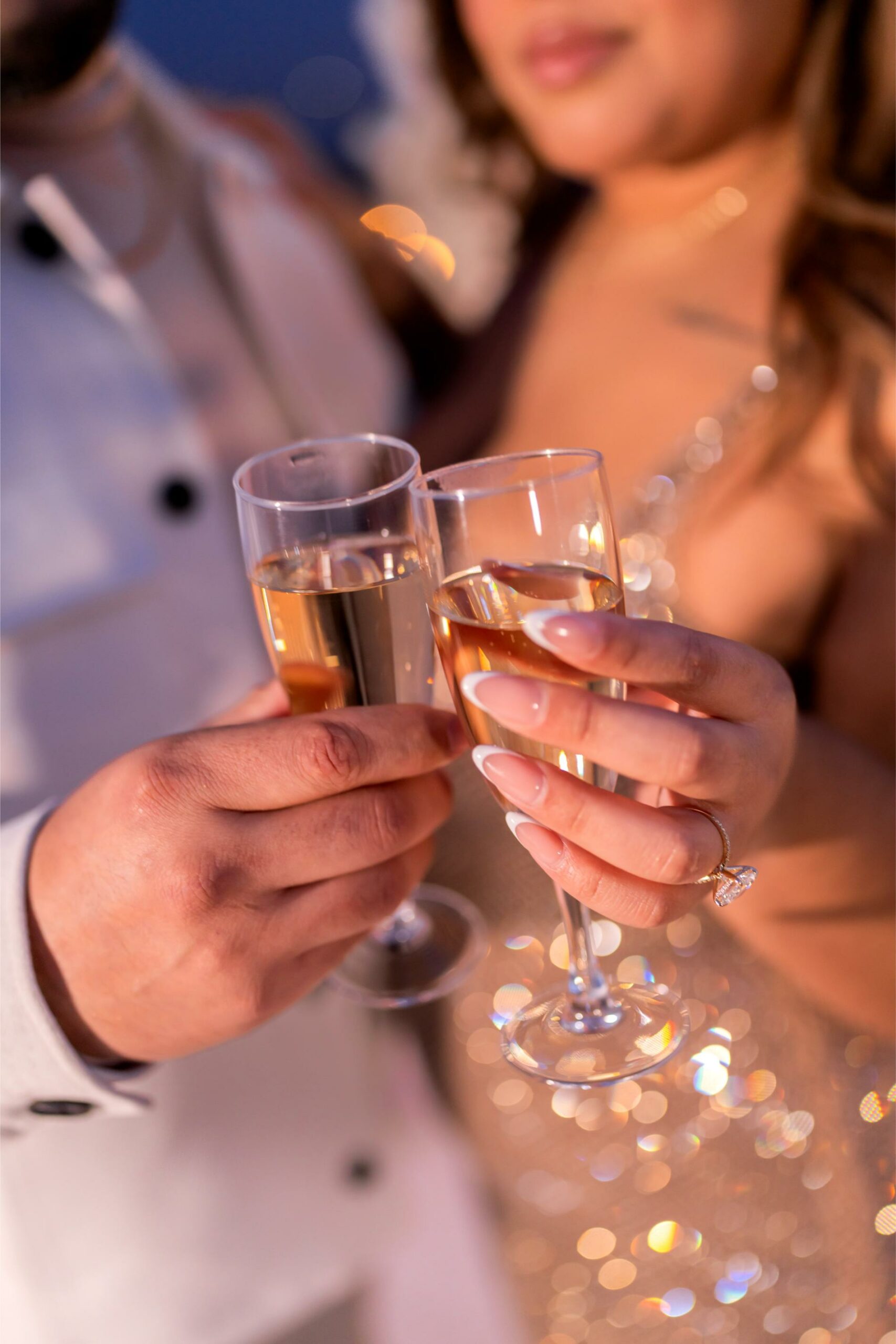 Newly engaged couple toasting with champagne glasses, engagement ring visible on her hand
