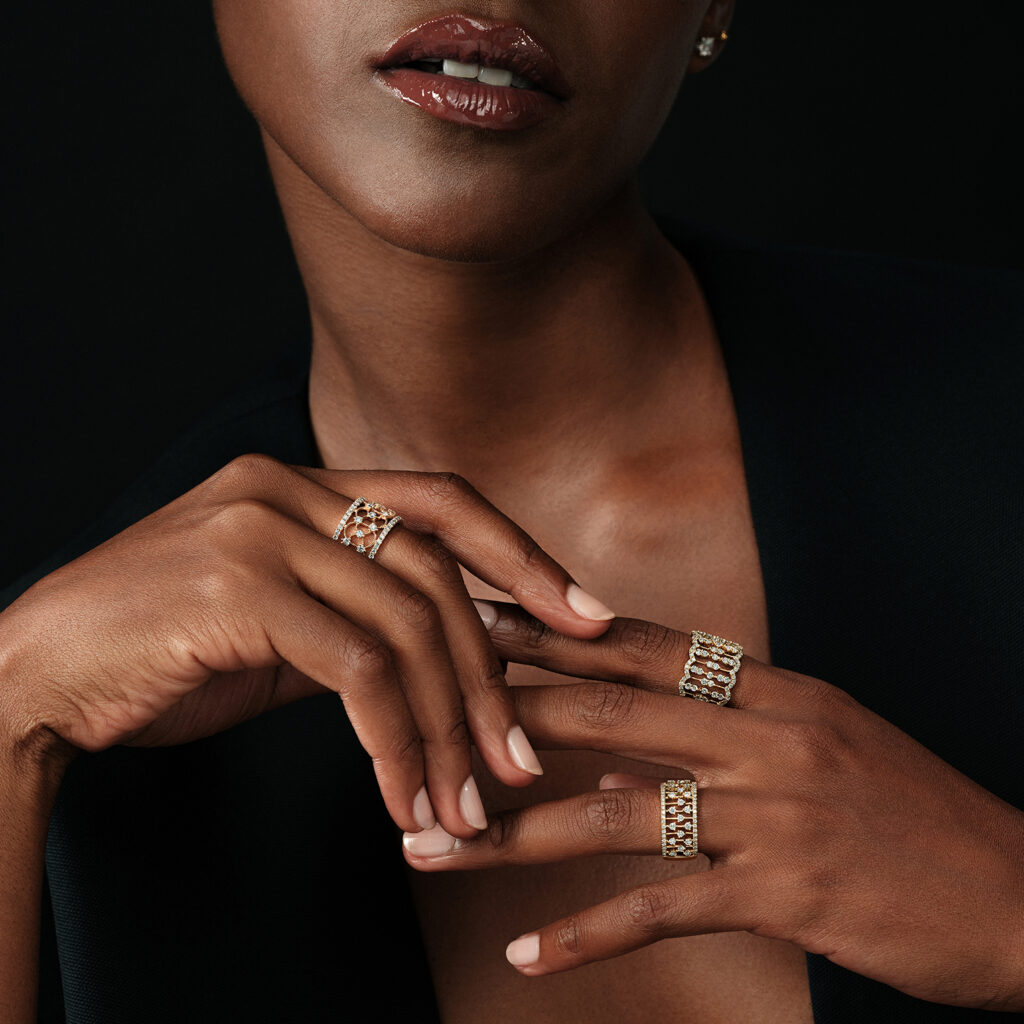 A woman wearing three Baunat wide-band diamond rings in yellow gold with intricate geometric openwork designs, showcasing bold and elegant engagement ring options available in Paris.