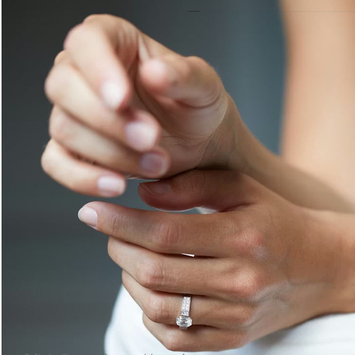 A woman wearing a white gold engagement ring featuring a large emerald-cut diamond with a pavé diamond band, an elegant and timeless choice for an engagement ring in Paris.