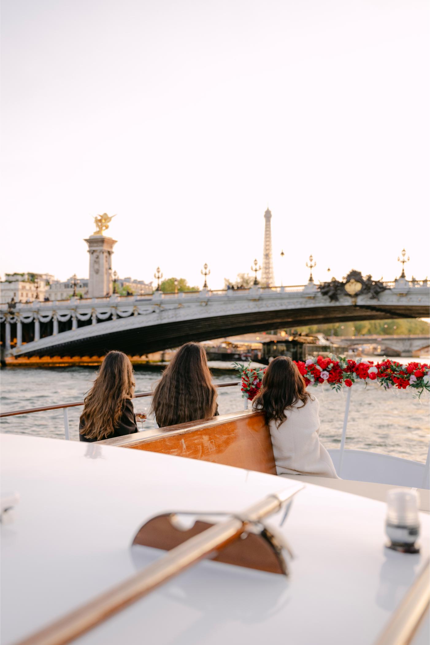 Trois personnes assises sur un bateau privatisé orné de fleurs rouges, face au Pont Alexandre III et à la Tour Eiffel sur la Seine à Paris