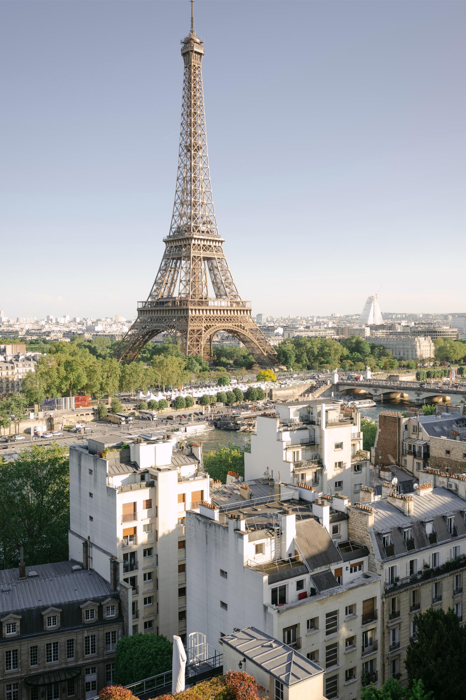 Aerial view of the Eiffel Tower from a rooftop in Paris, surrounded by Haussmann buildings, the Seine river and the city skyline on a clear day