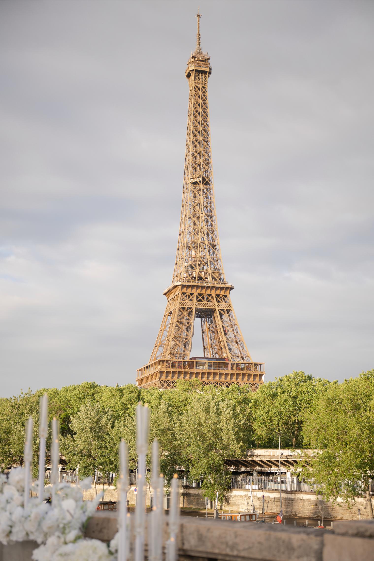 View of the Eiffel Tower from a proposal setup along the Seine in Paris, with white flower arrangements and tall candles in the foreground