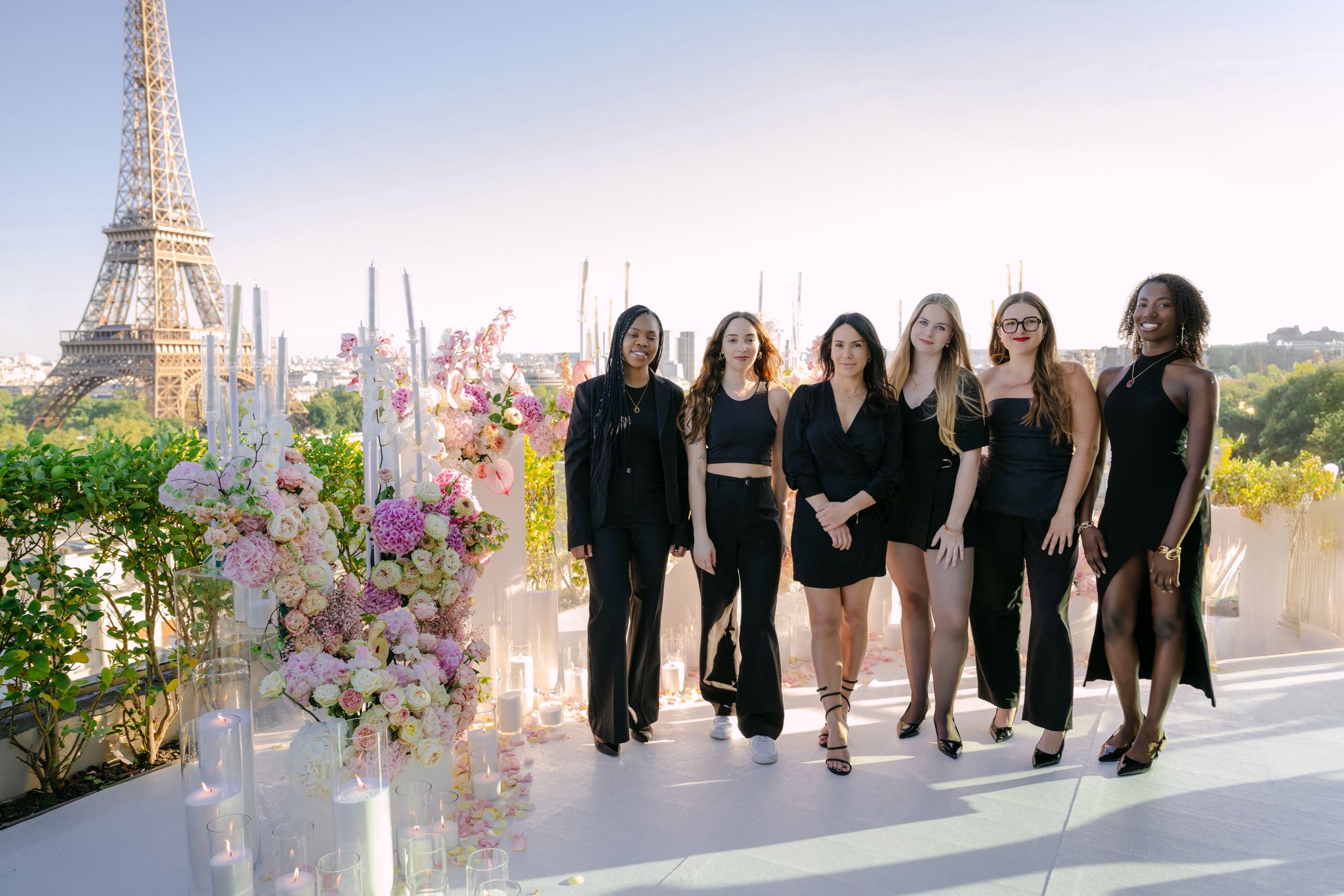 The Les Entremetteuses team of Paris proposal planners posing on a rooftop terrace with a floral arrangement, candles and a direct view of the Eiffel Tower in the background