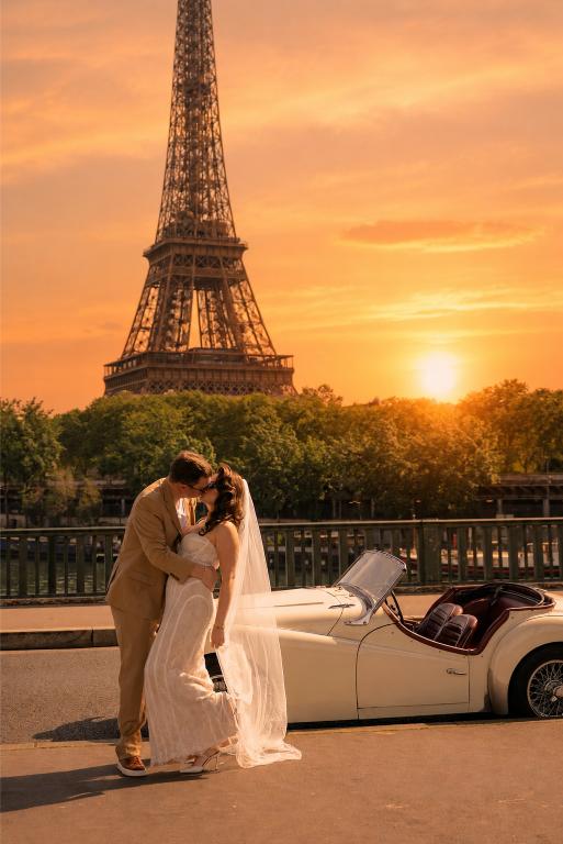 Couple kissing at sunset on the banks of the Seine in Paris with the Eiffel Tower in the background and a vintage white convertible car