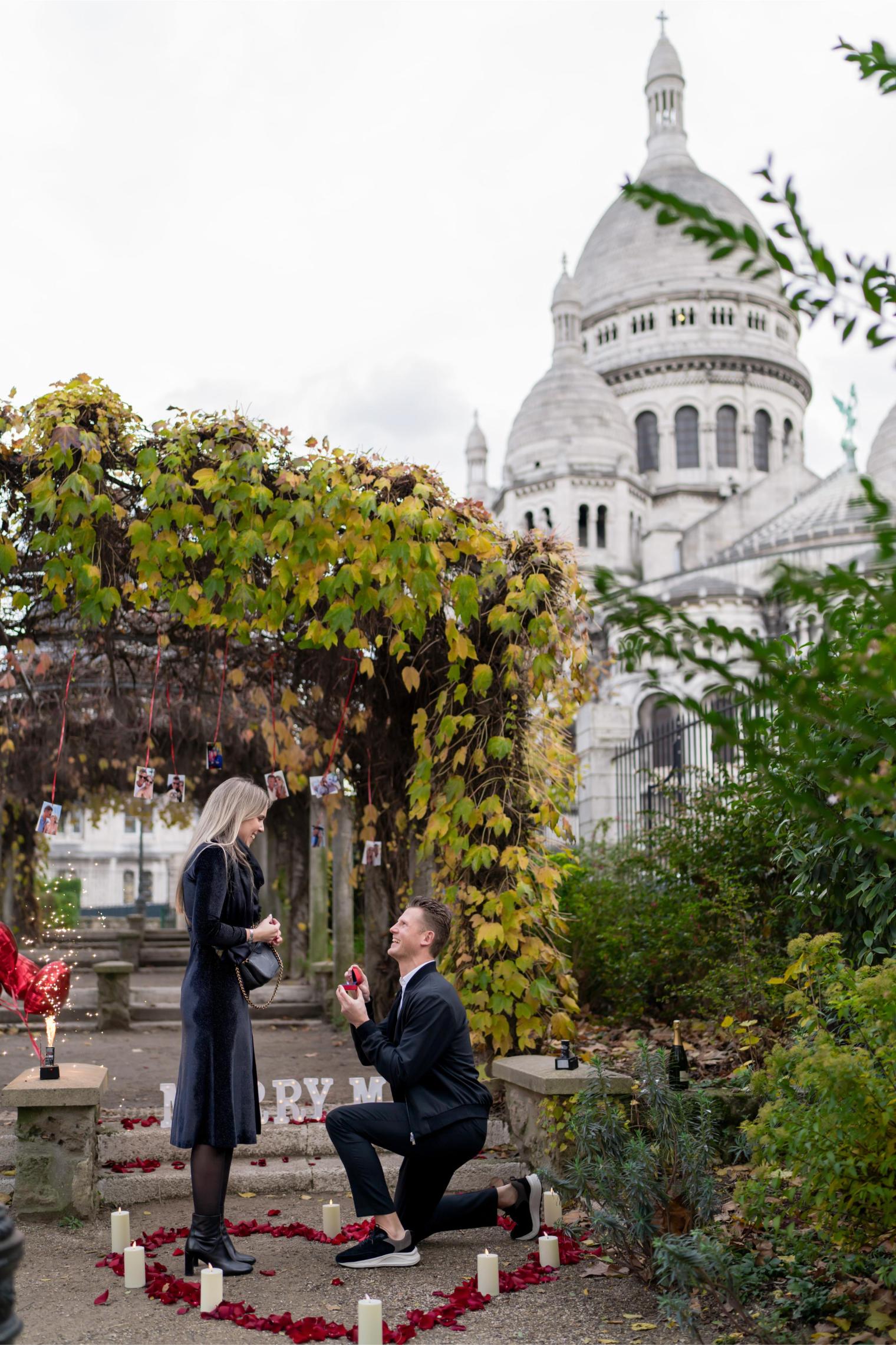 Man on one knee proposing in front of Sacré-Coeur in Montmartre Paris, red rose petals and candles on the ground