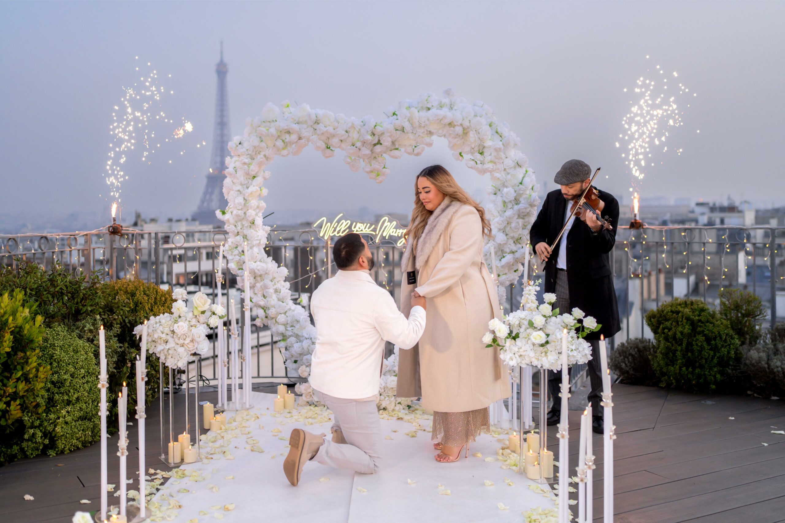 Demande en mariage sur un rooftop parisien avec vue sur la Tour Eiffel, arche florale blanche, bougies et violoniste