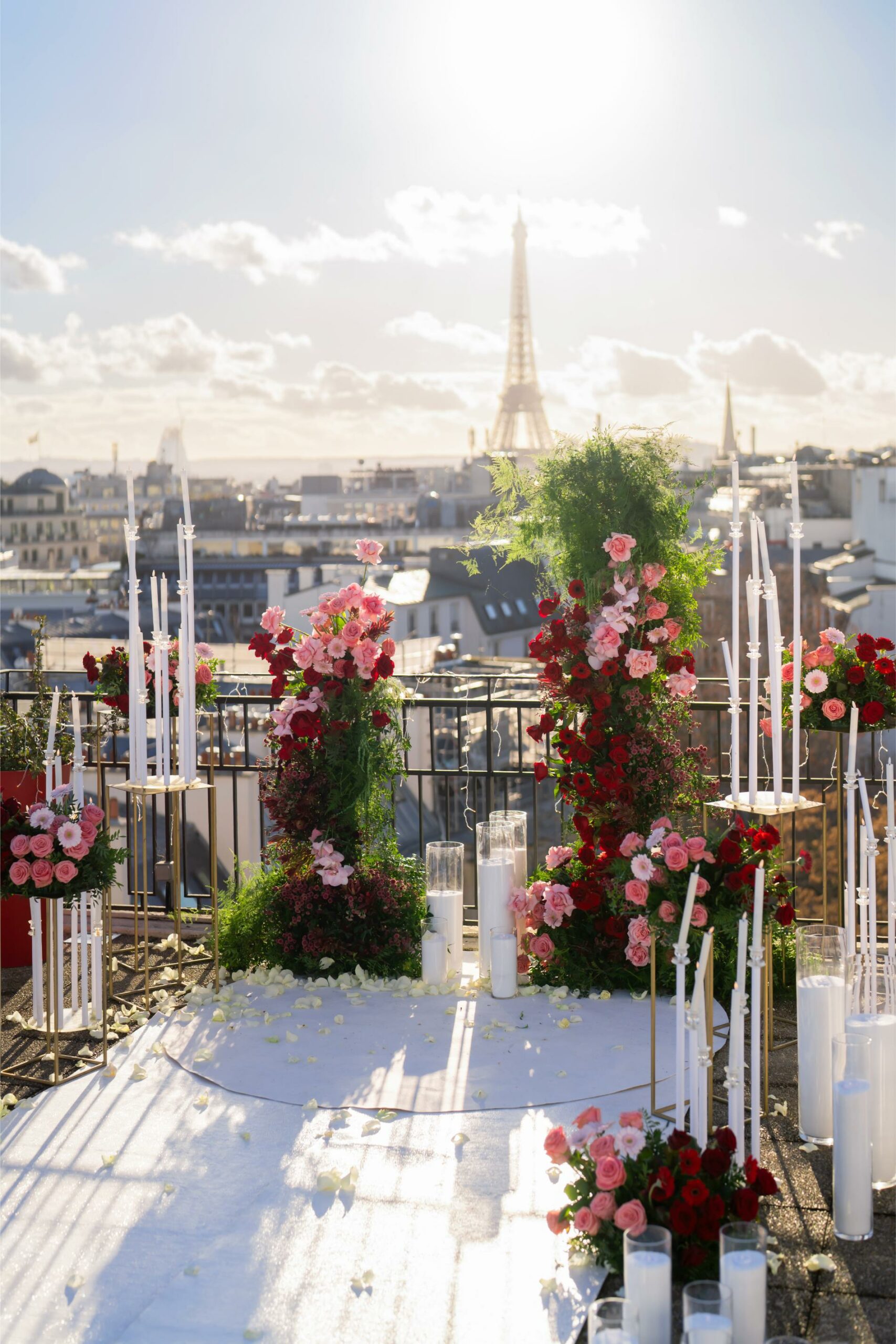 Proposal setup on a Paris rooftop terrace with pink and red floral arrangements, tall candles, and a view of the Eiffel Tower