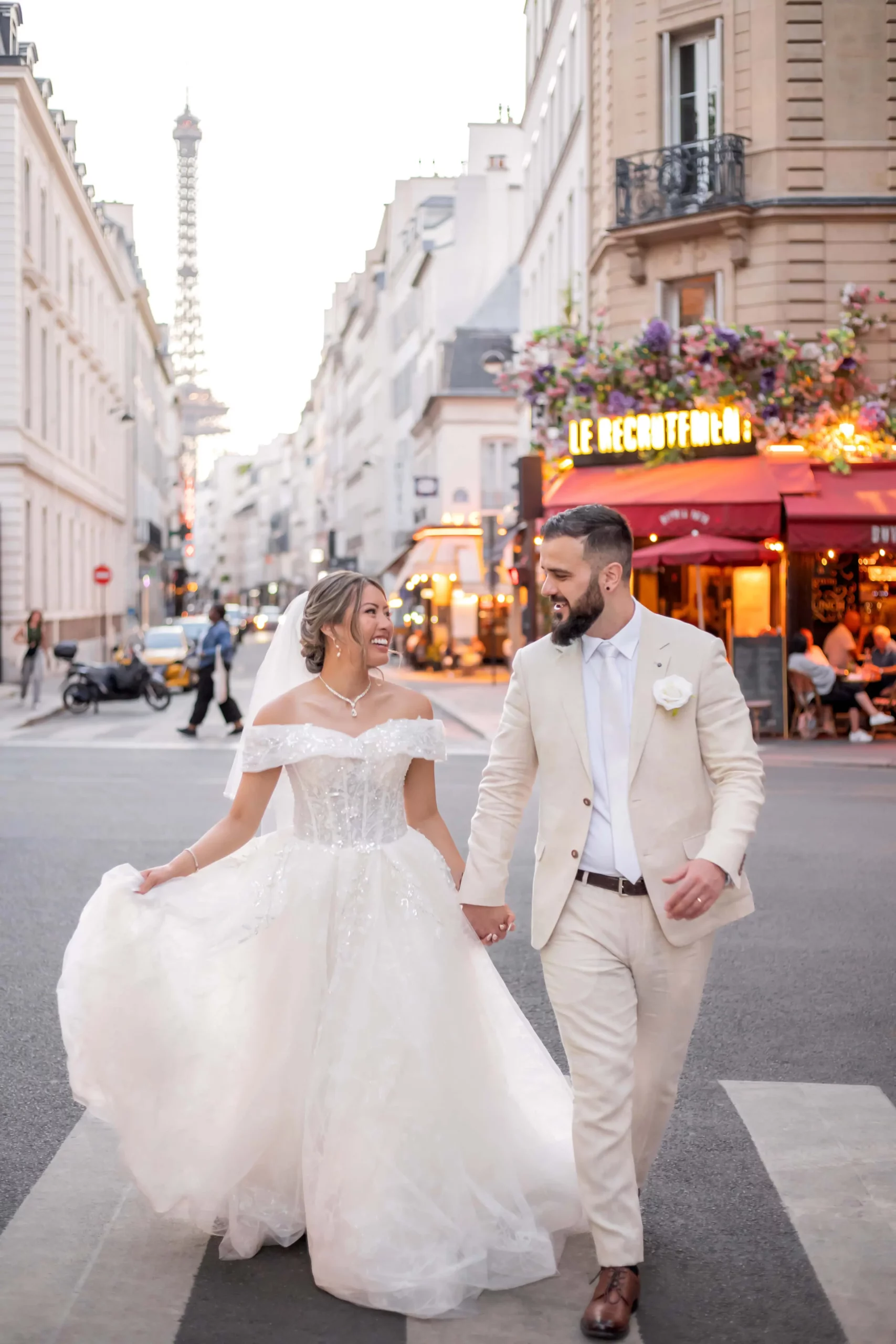 Bride and groom walking hand in hand through a Paris street with the Eiffel Tower in the background