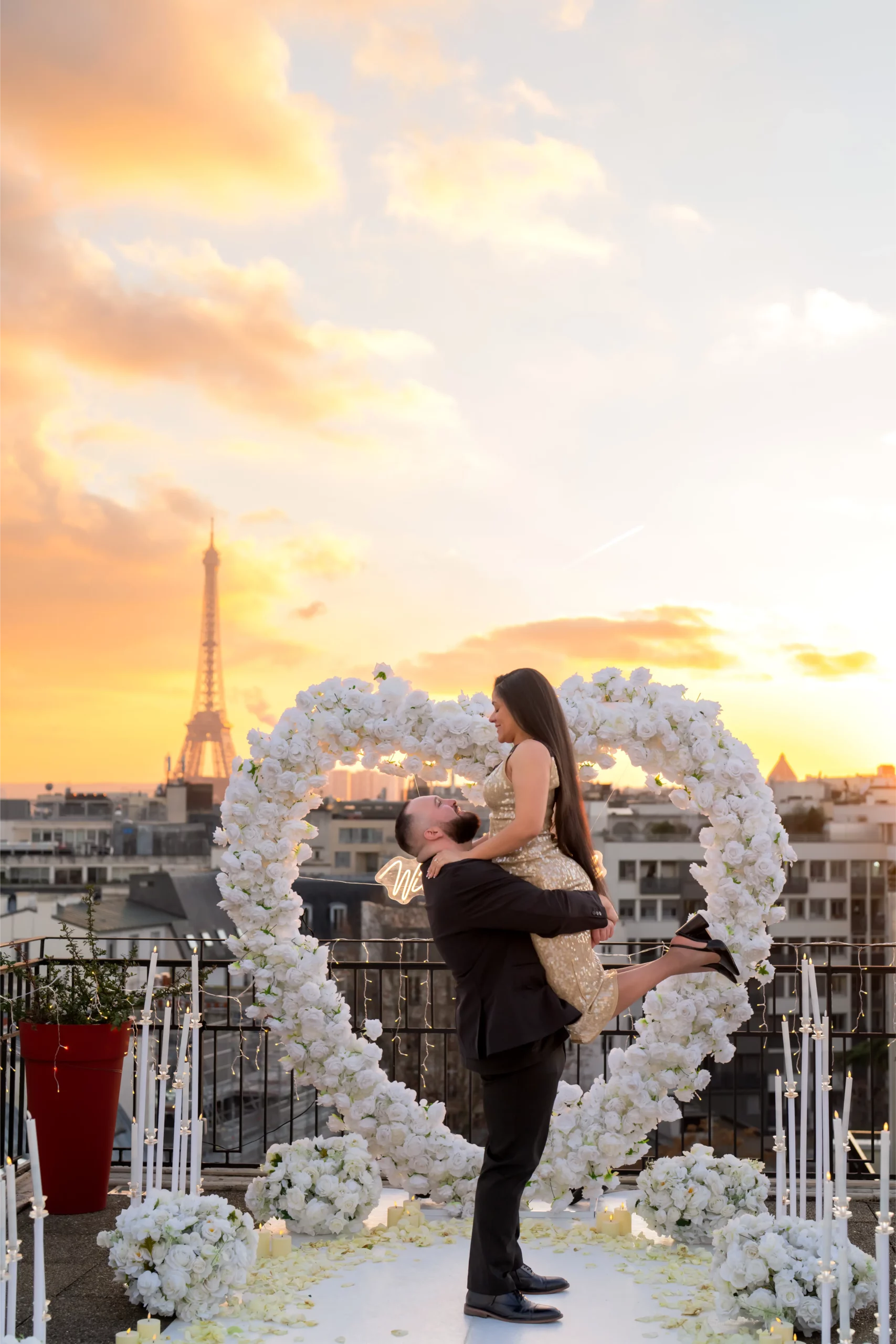 Couple embracing at golden hour on a Paris rooftop with Eiffel Tower view, surrounded by yellow roses and candles as the sun sets