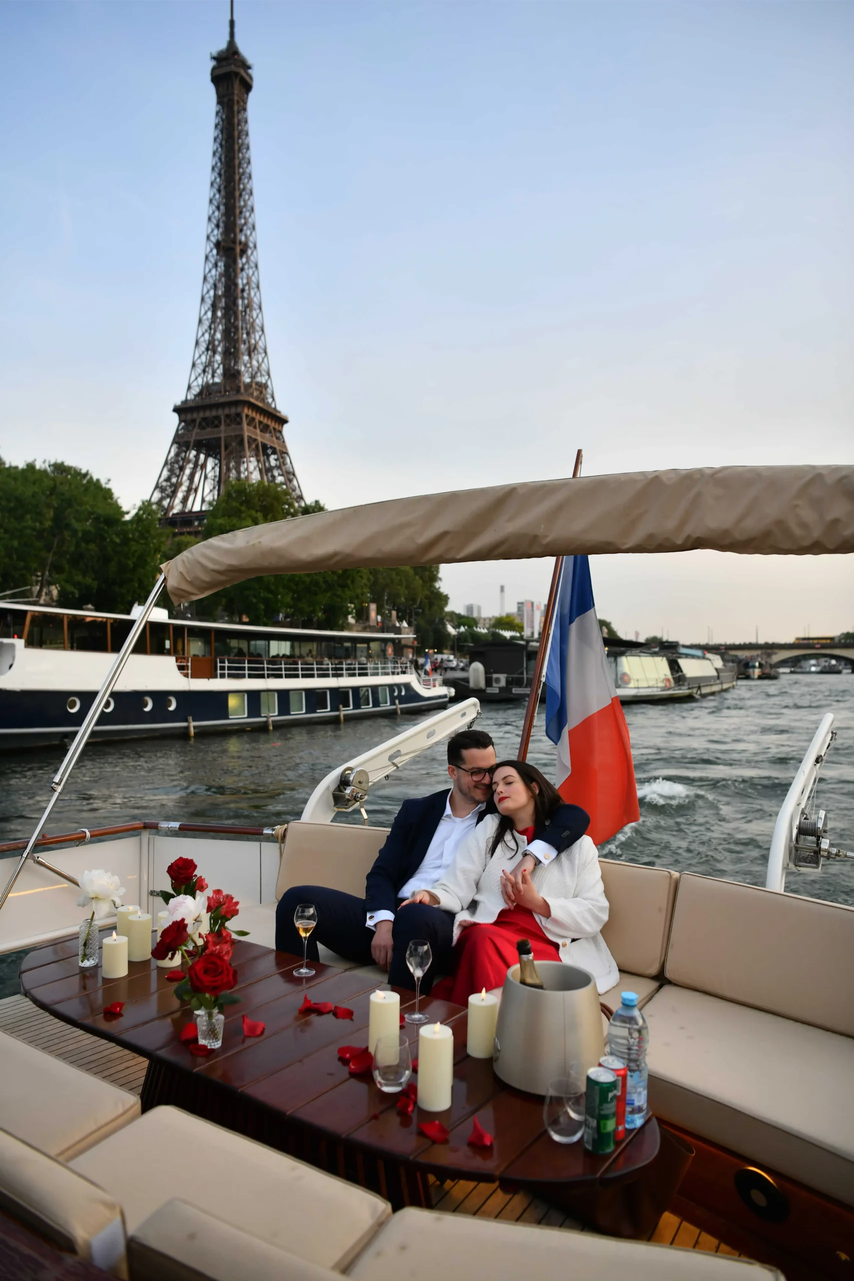 Couple relaxing on a private yacht cruising the Seine in Paris at dusk with the Eiffel Tower, red roses, candles and champagne on board
